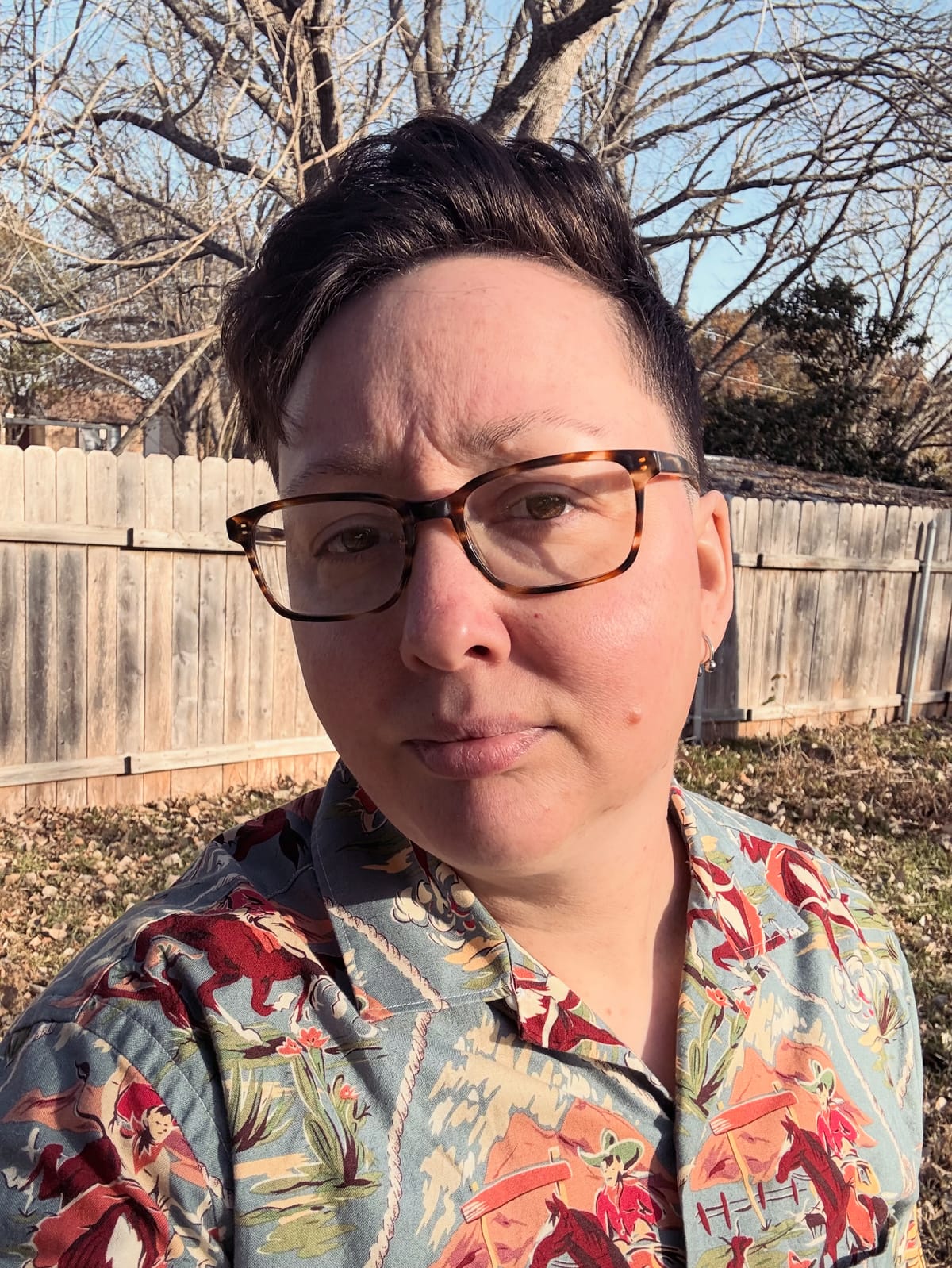 A selfie photo of me in my backyard, trying to look like a cool guy. I’m wearing a shirt either a retro cowboy print on it 